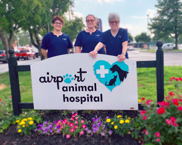Airport Animal Hospital team members pose by sign to welcome clients.